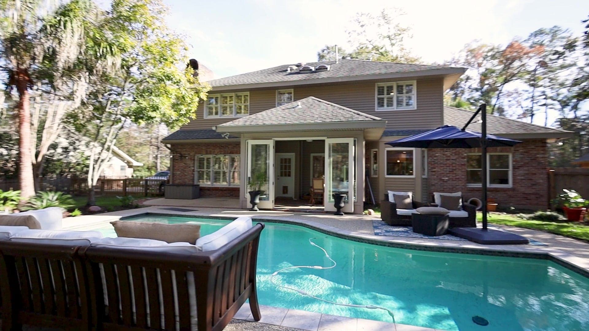 A brick-and-frame home behind a pool terrace, backed by pines and live oaks.