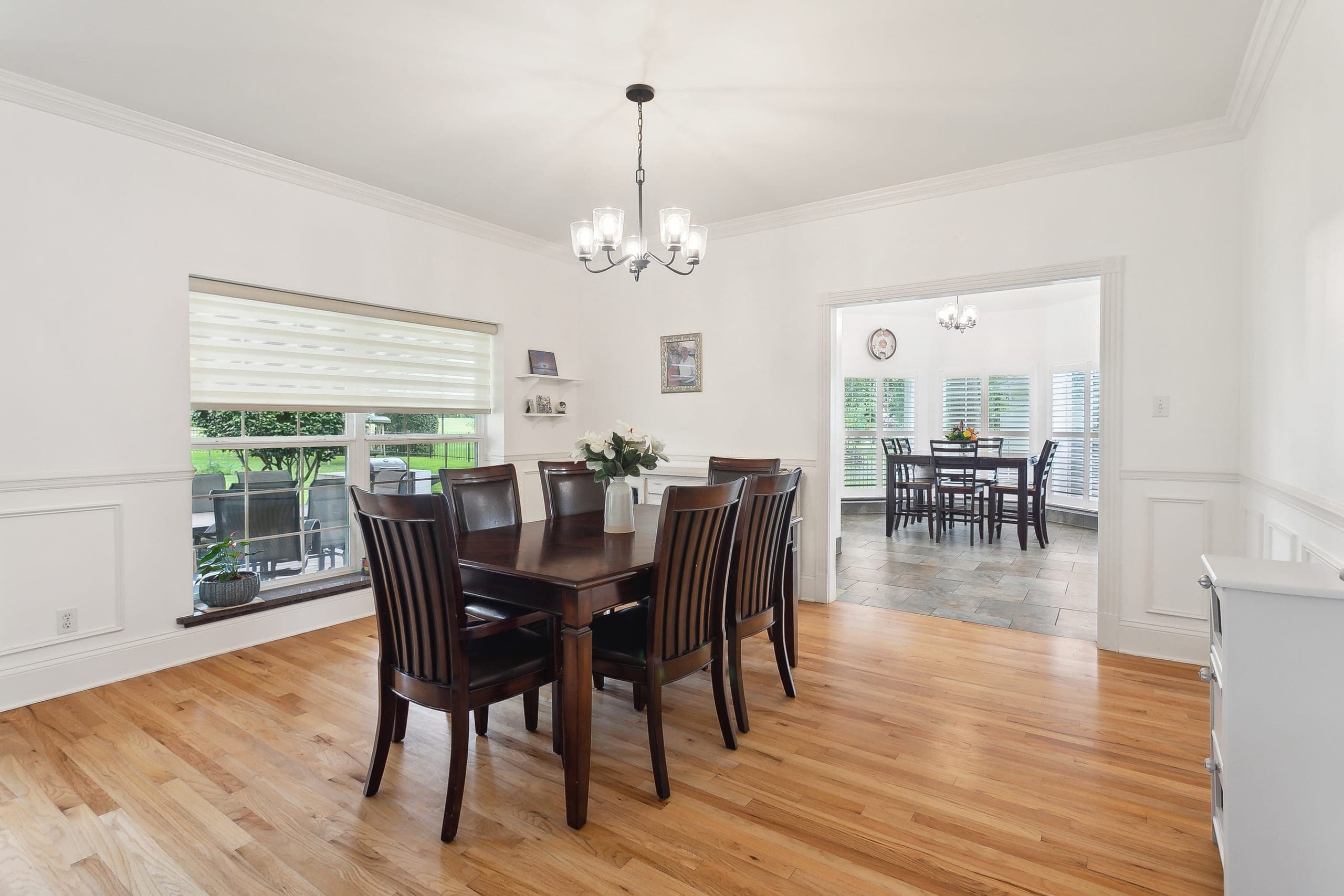 A dining room with oak floors, wainscot panelling, and a wide cased opening to the room beyond.