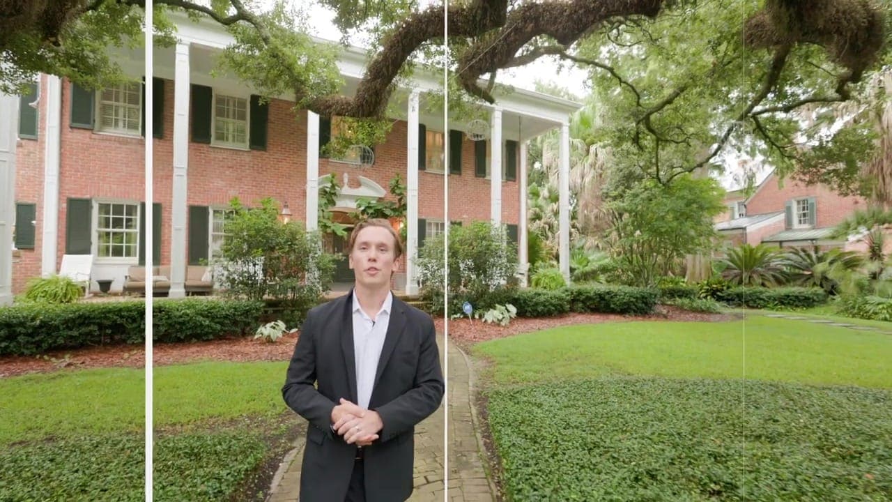Garrett Shearman speaking to camera on the front walk of a columned brick house beneath a live oak